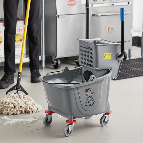 A man using a Lavex mop bucket with a caster to clean a mop.