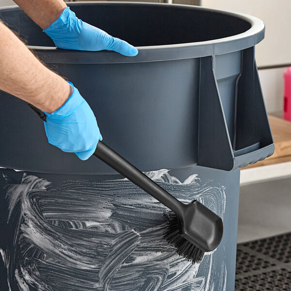 A person cleaning a trash can with a black floating utility brush.