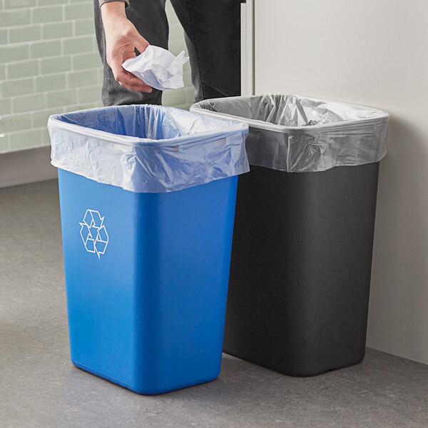 A man putting a crumpled paper into a blue and black Lavex rectangular trash can.