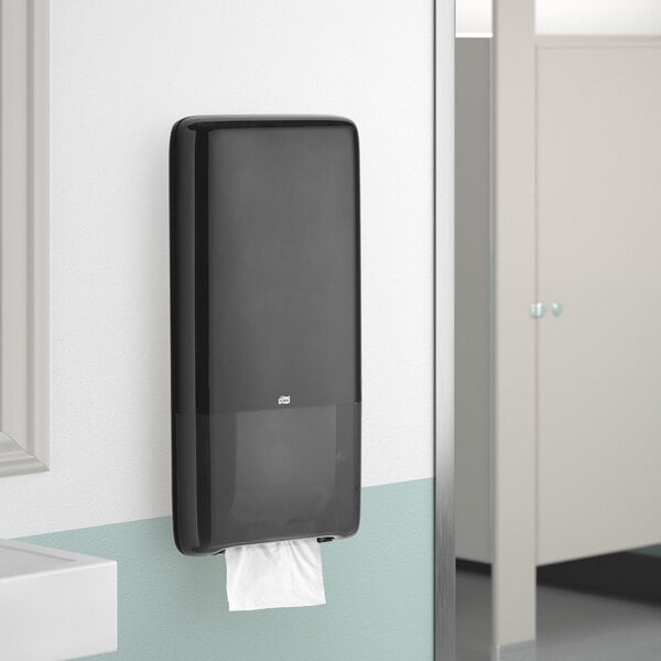 A black Tork PeakServe continuous paper towel dispenser on a wall.