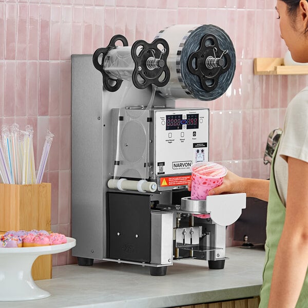 A woman using a Narvon automatic bubble tea sealing machine to seal a cup of pink liquid.