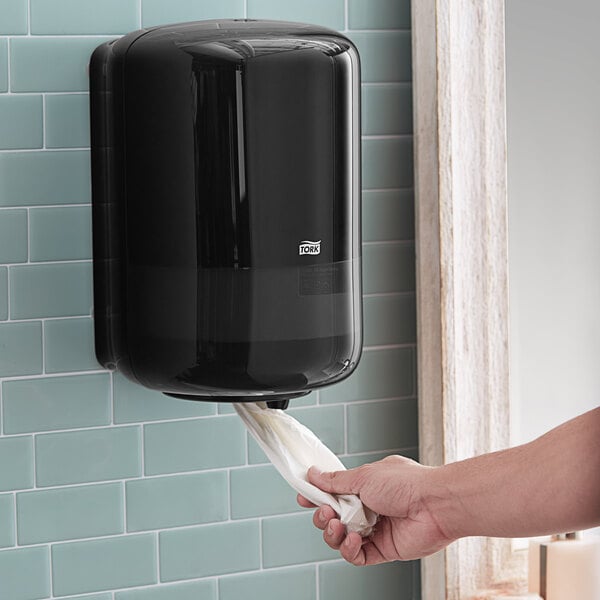 A person using a Tork wall-mount center pull paper towel dispenser.