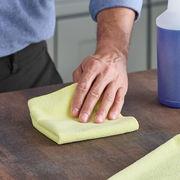 A hand wiping a table with a yellow Advantage Supplies microfiber cloth.
