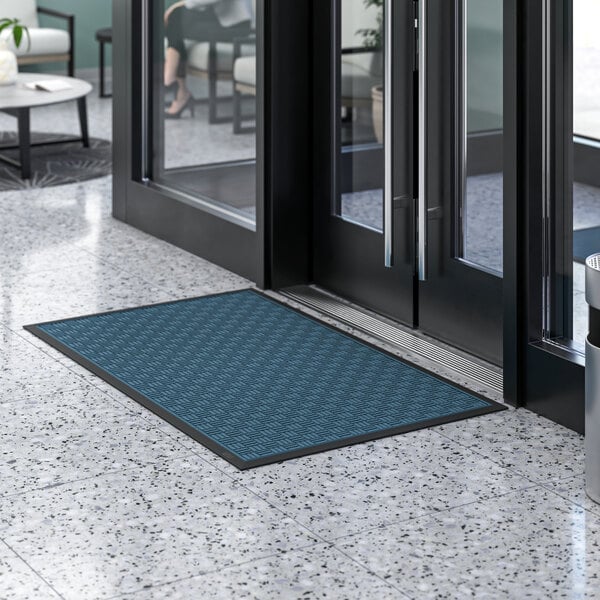 A blue and black Lavex Parquet entrance mat on a tiled floor in front of a glass door.