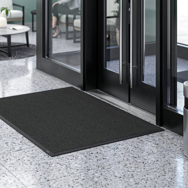 A Lavex black entrance mat on a marble floor in front of a glass door.