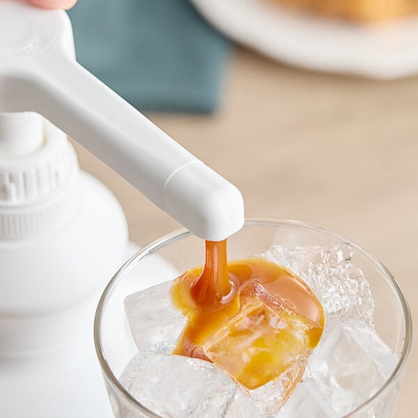 A person pouring Capora caramel sauce into a glass of ice.