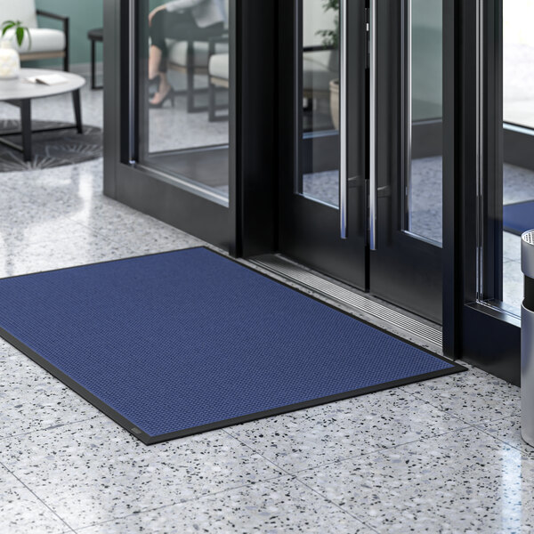A blue Lavex waffle entrance mat in front of a glass door.