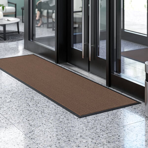 A brown Lavex Needle Rib entrance mat in front of a glass door.