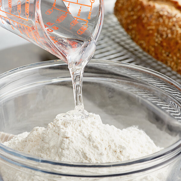 A clear liquid being poured into a bowl of white powder.