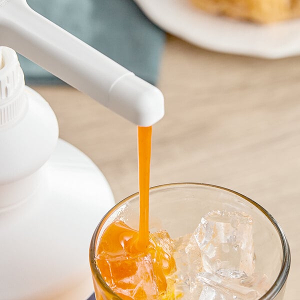 A glass of orange liquid with ice next to a white bottle of Capora Pumpkin Pie Flavoring Sauce.