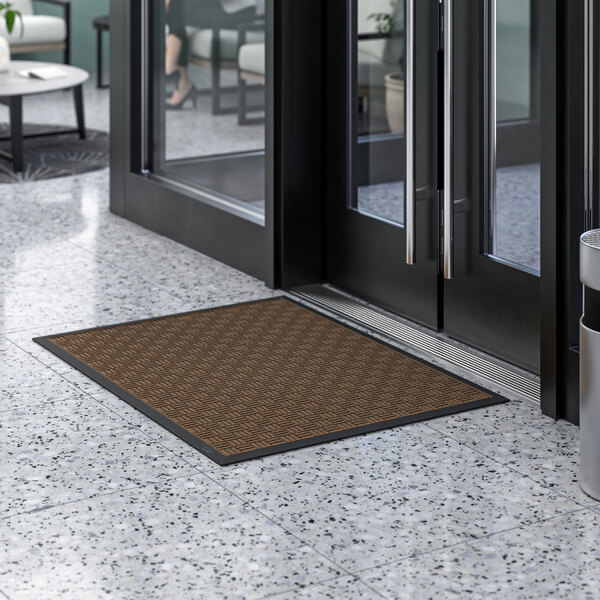 A brown Lavex parquet entrance mat on a white tiled floor next to a glass door.