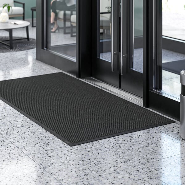 A black Lavex Needle Rib entrance mat on a marble floor.