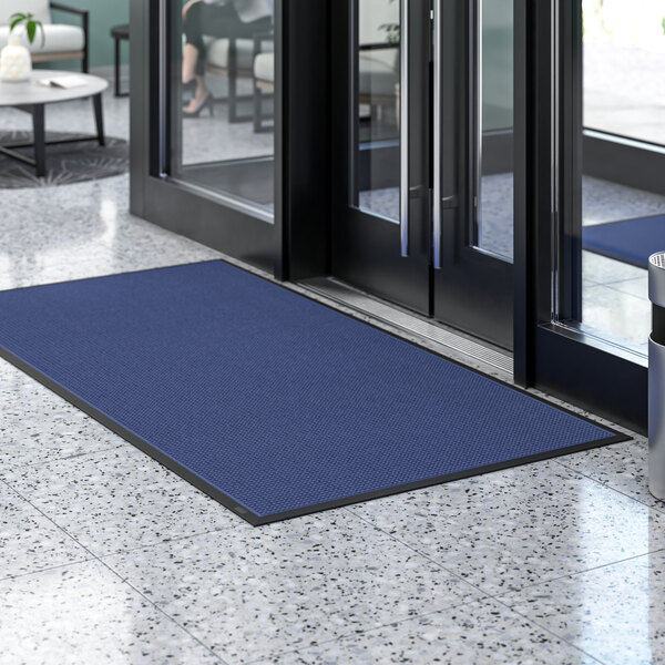 A blue Lavex waffle indoor entrance mat in front of a glass door.