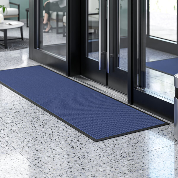 A blue Lavex Waffle entrance mat on a tiled floor in front of a glass door.