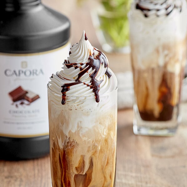 A glass of liquid with whipped cream and Capora chocolate sauce.