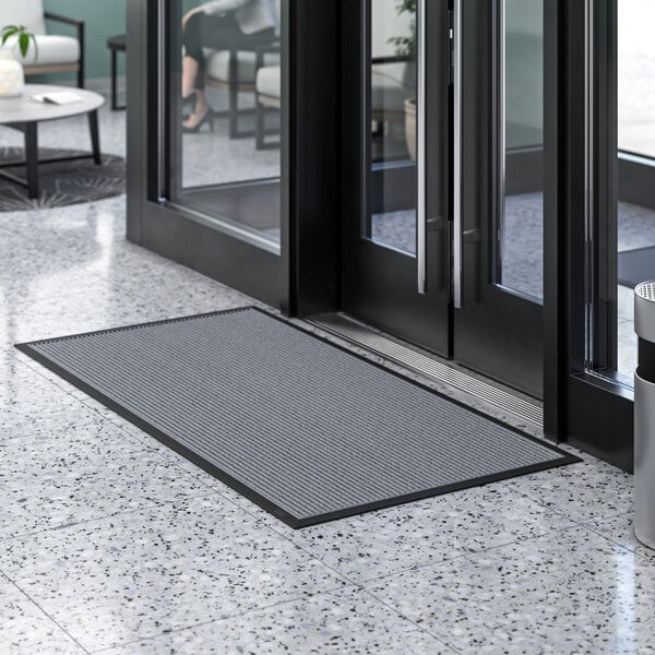 A gray Lavex Needle Rib entrance mat placed in front of a door.