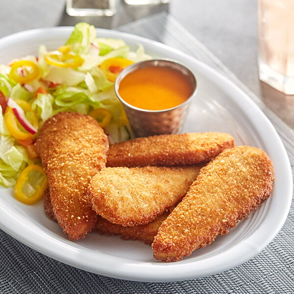 A plate of Dr. Praeger's Plant-Based Vegan Chick'n Tenders with a side of salad and sauce.