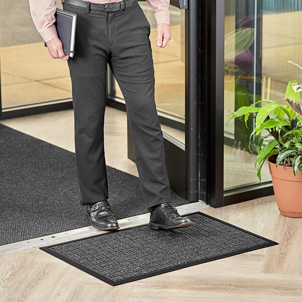 A man standing on a Lavex black parquet entrance mat holding a book.