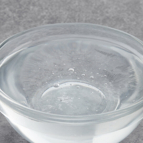 A clear glass bowl with clear liquid over a white background.