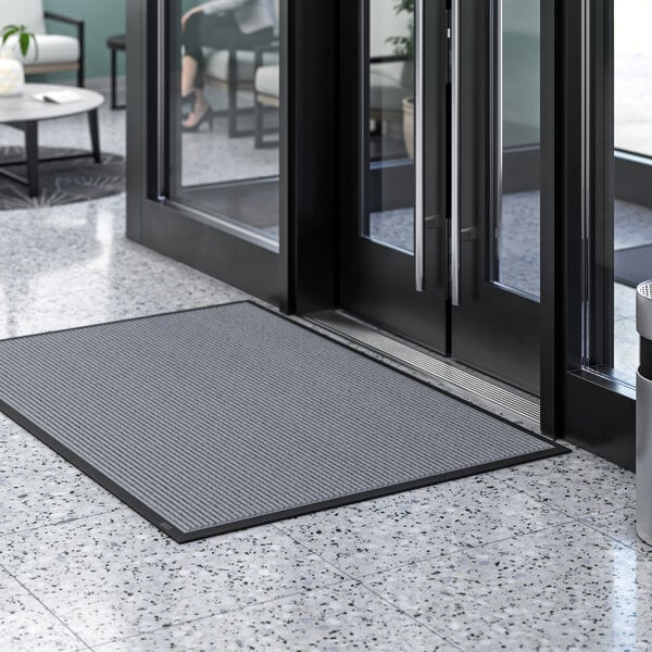 A grey rectangular Lavex indoor entrance mat placed in front of a door.
