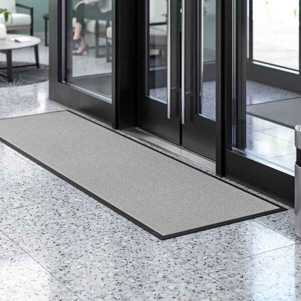 A large gray Lavex waffle entrance mat on the floor in front of a glass door.