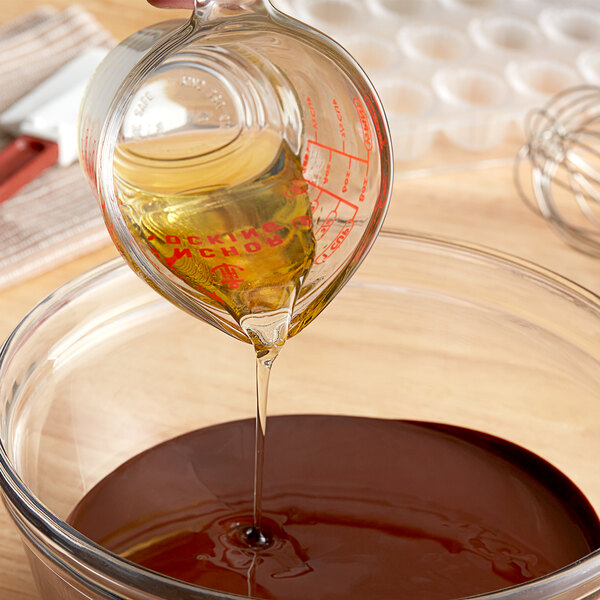 A person pours Malt Products Organic Agave Syrup into a bowl of chocolate in a home kitchen.