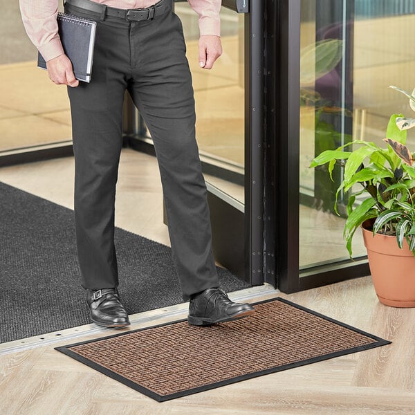 A man standing in front of a door with a brown Lavex Water Absorbent Parquet entrance mat.