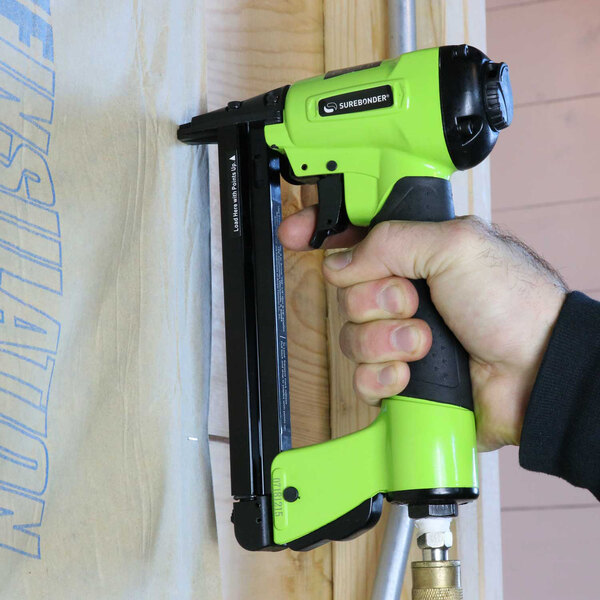 A hand holding a green and black Surebonder pneumatic staple gun.