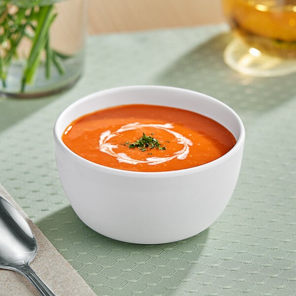 A white American Metalcraft melamine bowl of soup with a spoon on a table.