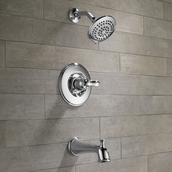 A Delta chrome faucet and shower kit on a tile wall.