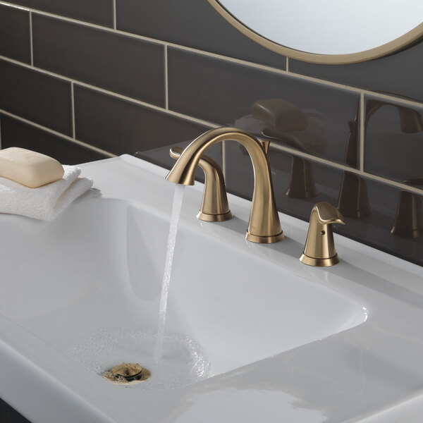 A white sink with a Delta Champagne Bronze widespread deck-mount faucet running water into it.