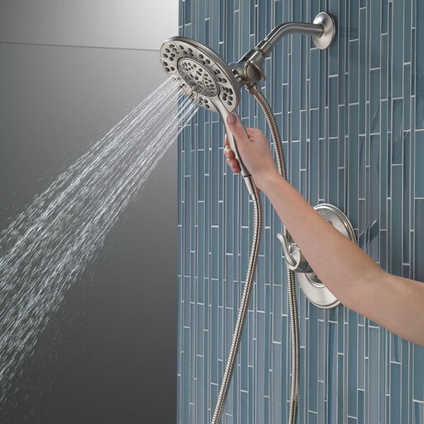 A hand holding a Delta stainless steel 2-in-1 hand shower and showerhead.