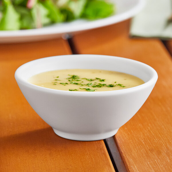 A white World Centric portion cup filled with soup on a table with green leaves.