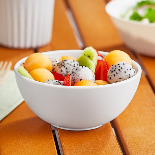 A close-up of a white World Centric ZeroWare bowl filled with fruit on a table.