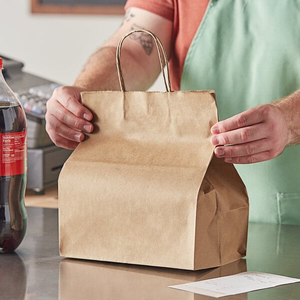 A person holding a Duro brown paper shopping bag with handles containing a soda.