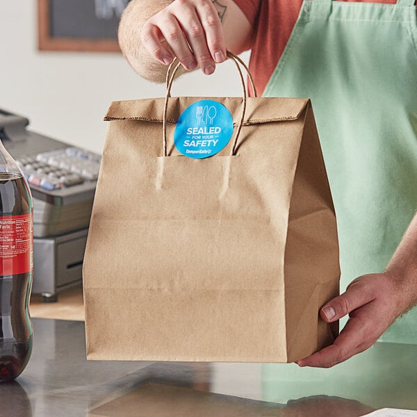 A person holding a Duro brown paper shopping bag with handles containing a soda.