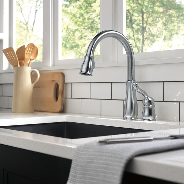 A Delta Leland kitchen faucet with a lever handle and pull-down spray wand over a sink on a white counter.