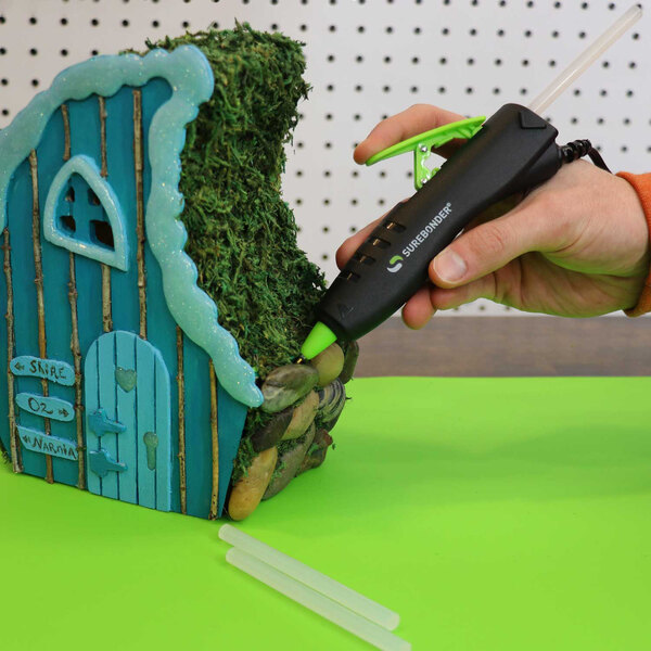 A person using a Surebonder high-temperature mini glue pen to make a house.