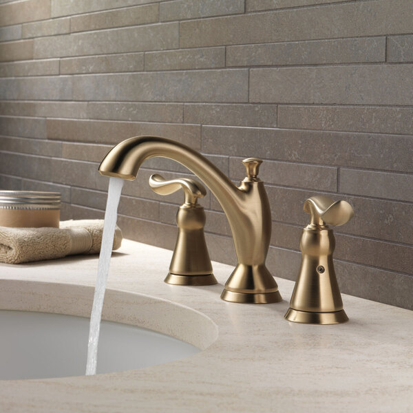 A Delta Linden widespread deck-mount faucet in matte champagne bronze with lever handles and a metal pop-up drain.