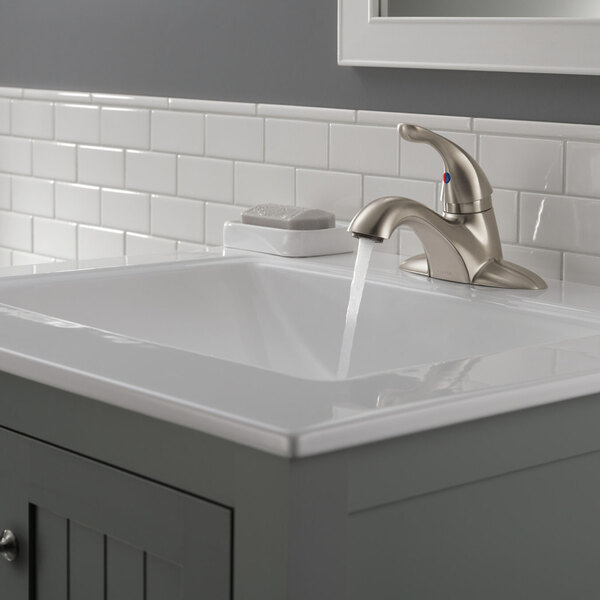 A Delta stainless steel deck-mount lavatory faucet with a metal pop-up drain on a sink.
