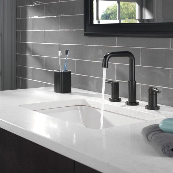 A bathroom sink with a Delta Matte Black Nicoli widespread deck-mount faucet running water.