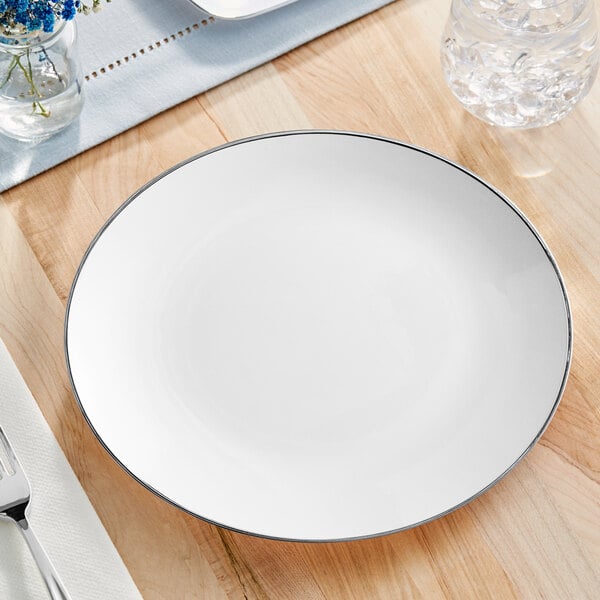 A Visions white plastic plate with a silver rim on a wood table.