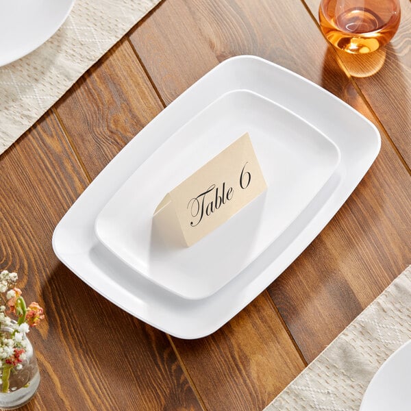 A close up of a Visions white rectangular plastic coupe platter on a table with a table number on it.