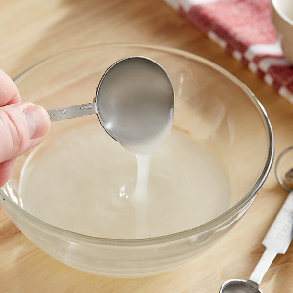 A person using a spoon to mix Nuvert Congealed Invert Syrup into a glass bowl.