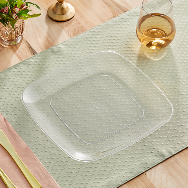 A Visions clear plastic square plate on a green placemat with a glass