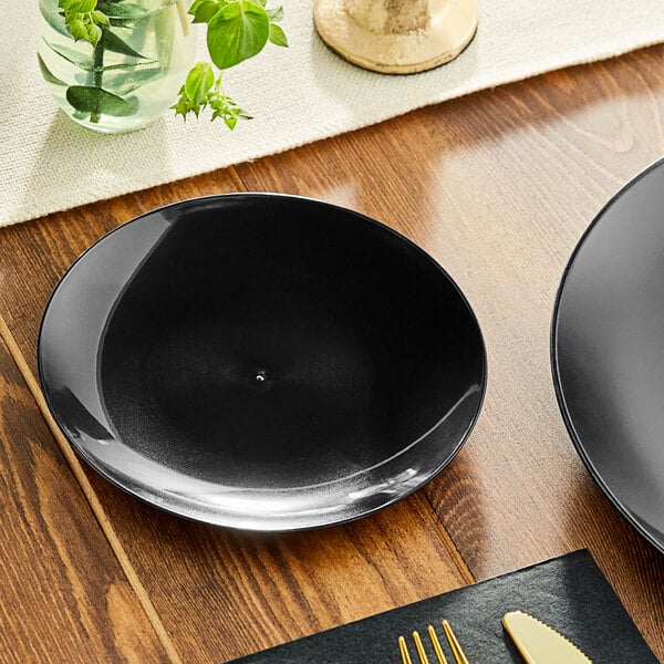 A black Visions plastic coupe plate on a wood surface with silverware.