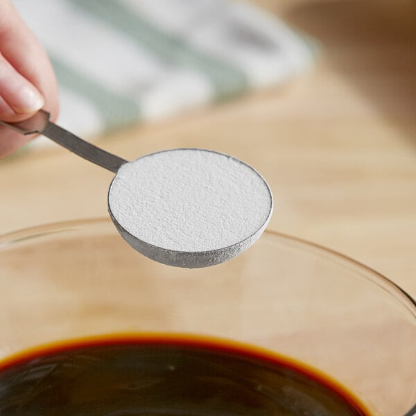 A person holding a spoon of white RiceRite syrup solids over a bowl of liquid.