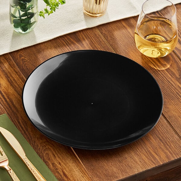 A black Visions plastic coupe plate on a wooden surface with a fork and knife.