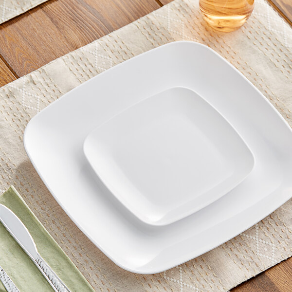 A white Visions square plastic plate with a knife and fork on a table.