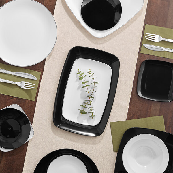 A table with white rectangular plastic plates with a silver border and silverware.